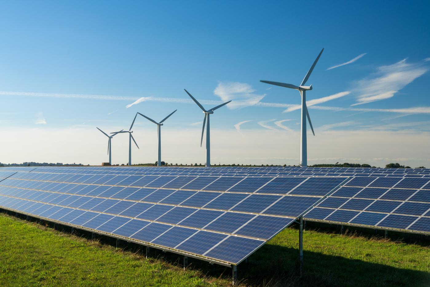 A renewable energy hub with solar panels in the foreground and wind turbines in the background